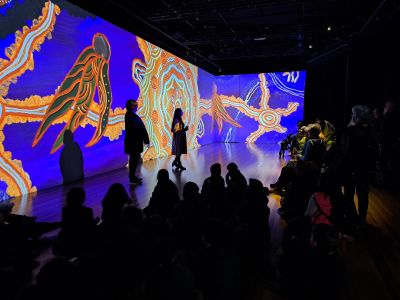 An artist standing in front of her artwork speaking to a room of people
